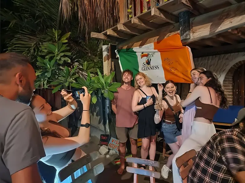 Viajeros posan con una bandera irlandesa firmada colgada del balcón de madera.