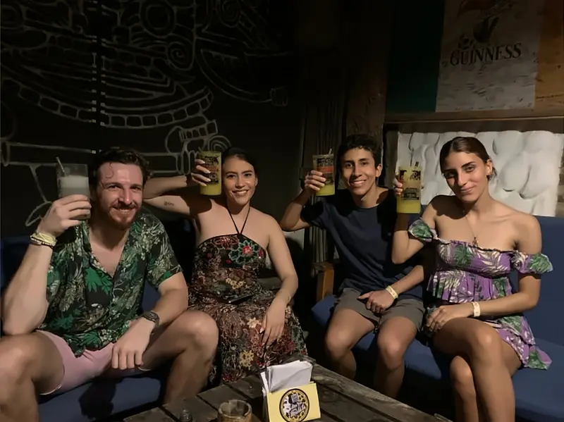 Cuatro amigos brindan con cócteles en los sofás del bar, junto a un mural de Guinness.
